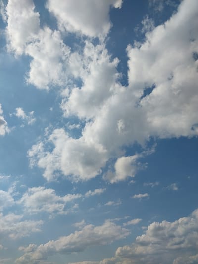 The image captures a bright blue sky filled with a variety of white, fluffy clouds, characteristic of a fair weather day. The clouds range from small, scattered puffs to larger, more dense formations. The lighting suggests it is daytime, possibly mid-morning or afternoon, with the sun illuminating the clouds from above, creating bright highlights and soft shadows. The image is a close-up shot of the sky, with no visible ground features or structures. The scene is static and serene, with no discernible activity. The location in Nizhneye Myachkovo, Russia, is implied but not visually represented in the image itself, which solely focuses on the sky.