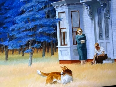 This image, located in the city of Reus, Spain, is a painting depicting a rural or semi-rural scene with a house, two people, and a dog.

In the background, a dense forest is rendered with vivid, almost electric blue foliage and dark, slender tree trunks. The ground beneath the trees transitions from a darker tone to a lighter, yellowish-green.

In the midground, a two-story white house with a reddish-brown foundation dominates the right side of the frame. It features a prominent bay window with dark window frames on the left and a recessed doorway on the right, adorned with decorative white corbels.

Two individuals are positioned near the house. A woman with light-colored hair, wearing a long-sleeved teal dress, stands facing forward to the left of the doorway, with her arms crossed. To the right of the doorway, a man with light-colored hair, wearing a short-sleeved white shirt and dark trousers, is seated on a low wall or steps. He leans forward, with his right hand extended towards the ground.

In the foreground, a medium-sized dog, resembling a Rough Collie or Shetland Sheepdog, stands facing right but looking back over its left shoulder towards the house. The dog has reddish-brown and white fur. The ground in the foreground is covered in dry, yellowish-brown grass.

There is no direct interaction depicted between the people or between the people and the dog. The overall impression is one of still observation within a stylized landscape.