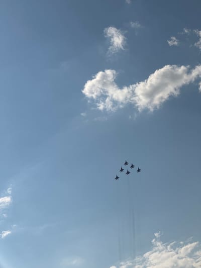 Six fighter jets fly in formation against a clear blue sky with scattered white clouds. The jets are dark in color and appear to be emitting smoke trails. The formation is in a diamond shape with one jet at the top, three in the middle, and two at the bottom. The scene is captured from a low angle, looking up at the sky. The image was taken in Nestiukovo, Russia.