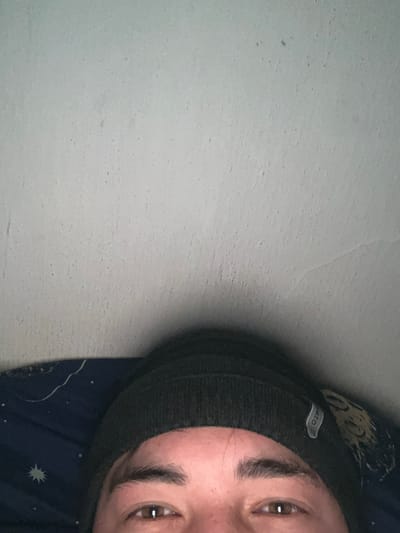 A close-up shot features a person wearing a dark gray beanie hat. The person's face is partially visible, showing eyebrows and eyes. The background is a textured gray surface. A glimpse of a navy blue fabric with a starry pattern can be seen near the bottom of the frame. The image is rotated, positioning the person's face on the right side.