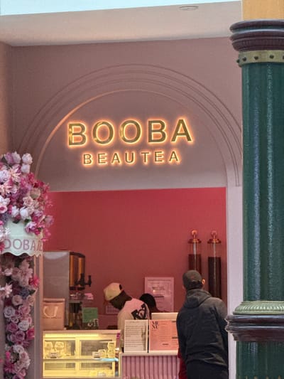 The image shows the entrance to a business called "BOOBA BEAUTEA". The interior decor includes a pink wall, neon lettering, and flower decorations. Customers can be seen at the counter. The location is likely in Milnerton, South Africa.