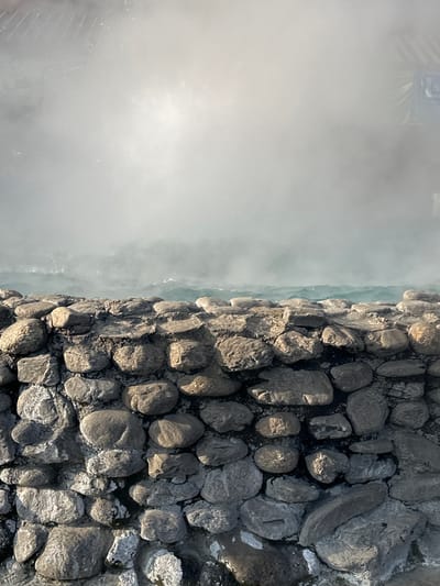 A dense fog envelops the left side of the image, obscuring the view. A stone wall composed of various-sized, gray rocks runs vertically along the right side. The texture of the rocks is rough, with visible crevices and variations in color due to light and shadow. The fog and stone wall create a contrasting visual effect.