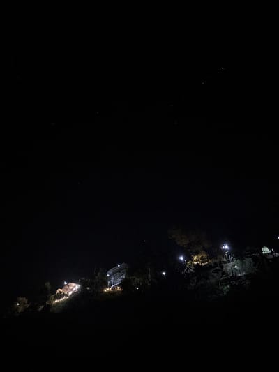 The image shows a nighttime scene in Khlong Khian, Thailand, with several illuminated structures. The structures appear to be elevated and interspersed with trees or vegetation. The lighting suggests possible residences or commercial establishments. The overall scene has low ambient light.