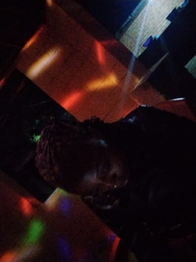 The image appears to capture a dimly lit scene, possibly at night, with colorful lights creating an abstract pattern across the frame. The primary subject is a large, dark, amorphous shape in the foreground, which is difficult to discern clearly due to the low light and the quality of the image. It might be an object or a creature. The background is a mix of dark areas and geometric shapes of light, suggesting an artificial environment, perhaps an indoor space with projected lights or a scene with light reflections. Some areas show what looks like a tiled surface, possibly a floor or wall, illuminated by streaks of orange and white light. There are also patches of red, green, and purple light scattered throughout the image, further contributing to the abstract and somewhat chaotic visual. No people are clearly visible. The overall impression is one of mystery and visual abstraction, with the lack of sharp detail making it hard to pinpoint specific objects or activities. The setting is unclear but the presence of the colored lights and the textured surfaces hint at a place where such lighting effects might be employed, such as a party venue, a stage, or even an artistic installation. No text is visible.