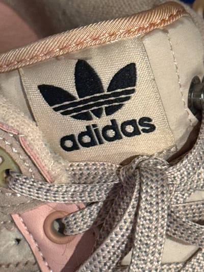 The image shows a close-up of an Adidas shoe. The Adidas logo is prominently displayed on a tag. The shoelaces are gray and knotted. Other details include the shoe's fabric, stitching, and metallic eyelet. The image does not include any information to suggest a location in Kladovitsy, Russia.