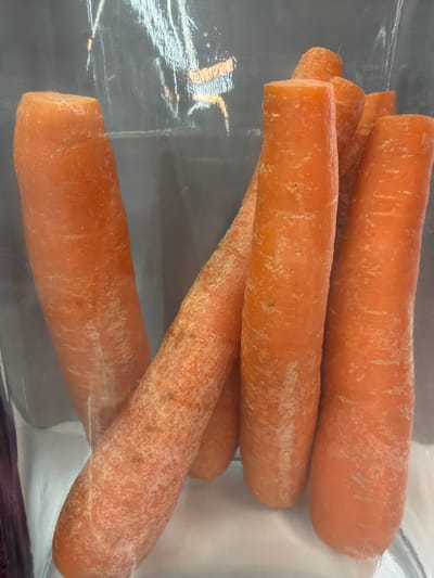 The image shows several unpeeled, orange carrots in a clear plastic bag. The carrots appear to be fresh. The specific location in Arinj, Armenia, is not discernible from the image.