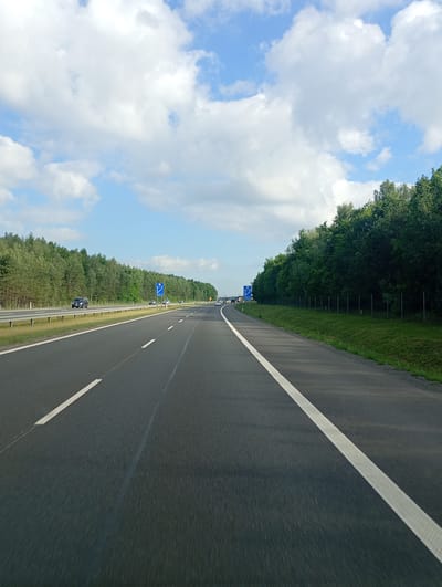 The image shows a highway in Mysłowice, Poland, with a cloudy sky and trees lining the sides. The highway is paved with asphalt and has white lines marking the lanes. There are cars on the highway, and traffic signs are visible. The overall scene suggests a typical day on a highway, with moderate traffic and clear weather.