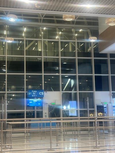 The image depicts the interior of an airport in Addis Ababa, Ethiopia. The focal point is a gate sign for gate C5, which is written in both English and Chinese. A digital display panel beside the sign shows flight information, including flight times, destinations, and gate information. The interior architecture features a grid-like pattern created by metal supports and large windows. There are hanging light fixtures in the distance on the left side of the image. A set of metal bars is shown on the right side of the image.