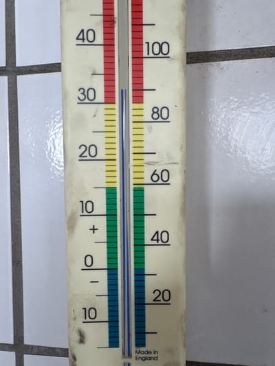 The image shows a close-up, eye-level, slightly angled outdoor shot of a thermometer. The thermometer is a vertical, elongated object with numerical markings and colored segments. It is positioned against a background that appears to be a tiled wall, with horizontal and vertical grout lines visible.
The thermometer itself is cream-colored and has markings from 0 to 100, with increments of 10. There are also markings for negative temperatures, down to -10. The thermometer displays a red liquid column reaching up to approximately the 40 mark, a yellow liquid column reaching up to approximately the 70 mark, a green liquid column reaching up to approximately the 50 mark, and a blue liquid column reaching down to approximately the -5 mark. This multi-colored liquid likely indicates different temperature ranges or functions, such as ambient temperature, hot water temperature, or pool temperature.
The text "Made in England" is visible at the bottom of the thermometer.
The specific location in the city of Wettstetten, Germany cannot be determined from the provided image. The image lacks any identifying landmarks, street signs, or other contextual clues that would pinpoint its geographical location within Wettstetten.
