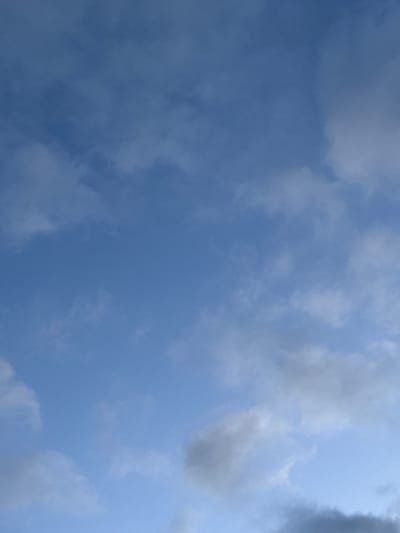The image shows a clear blue sky with scattered white and gray clouds. The clouds are wispy and appear to be moving, suggesting a breezy day. There are no people or objects visible in the image, and the focus is entirely on the sky. The scene is natural and serene. It's impossible to determine the location within Santiago de Compostela based solely on this image, as it depicts a generic sky.