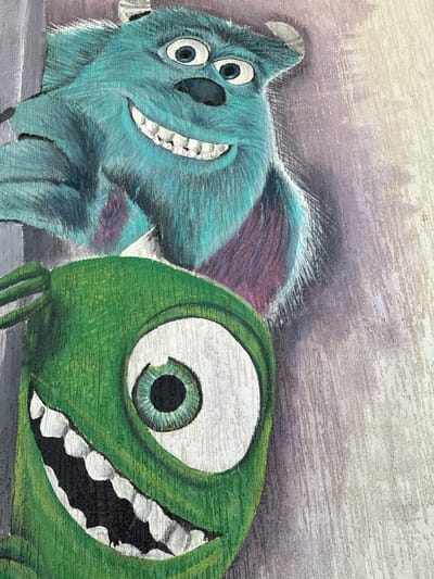 A close-up, medium shot depicts the characters James P. "Sulley" Sullivan and Mike Wazowski from the film *Monsters, Inc.* Sulley, a large blue-furred monster with a purple back, is on the left, while Mike, a green, one-eyed monster, is on the right. Both characters are smiling broadly, displaying their teeth. The background consists of muted, brush-stroked colors, transitioning from gray to white at the top. The artwork appears to be painted on a textured surface. There is no evidence to indicate that this image was taken in Safaga, Egypt.