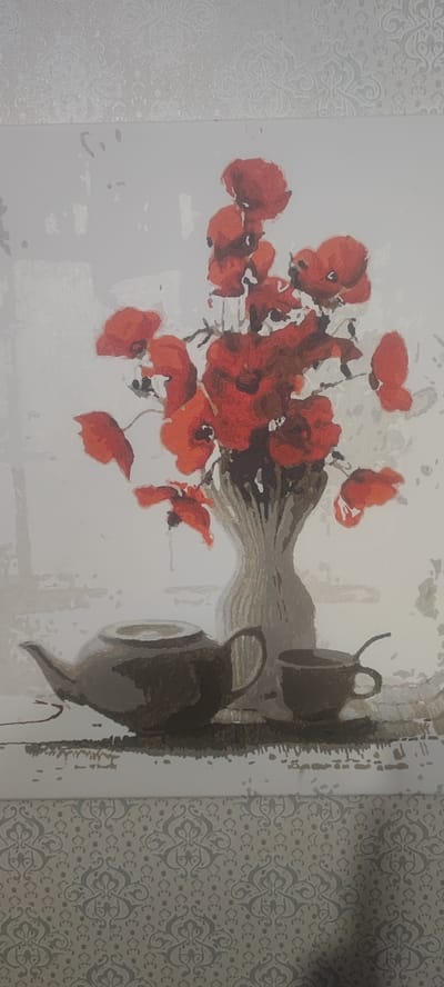 The image depicts a still life painting featuring a bouquet of red poppies in a textured vase, placed on a surface next to a teapot and a teacup. The background is a light color with abstract white shapes. The bottom of the image shows a patterned wallpaper. There is no discernible location in Svitlovodsk, Ukraine, nor any indication of activity or interaction. The scene is static and appears to be a work of art.