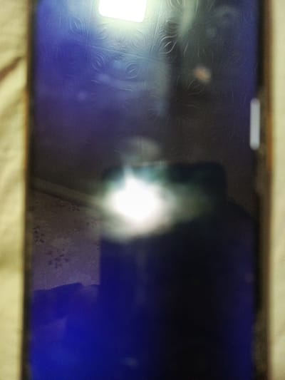 The image shows a dark, blurry surface with bright reflections. The surface appears to be a screen, possibly of a smartphone or tablet, with a light source reflecting off it. There is a textured pattern visible on the surface, likely a background or screen saver. The lighting conditions suggest the photo was taken in low light or with a strong light source directed at the screen. The image does not contain any discernible elements that would allow for identification of a specific location within Svoboda, Russia, or any details about people or actions.