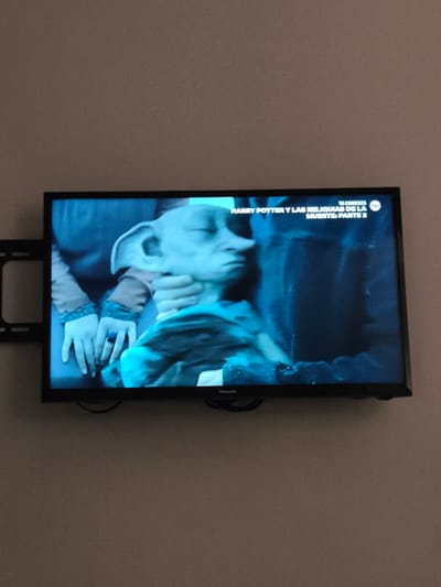 A television mounted on a wall displays a scene from "Harry Potter y las Reliquias de la Muerte: Parte 2." The scene features a character resembling Dobby, the house-elf, being held. The TV is a Hisense brand. The setting is unknown, but the location is Guatemala City, Guatemala.