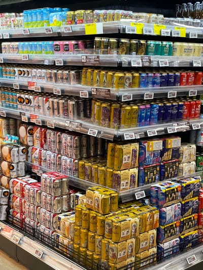 This is a photograph of a refrigerated section of a store, likely a supermarket or liquor store, featuring a variety of Japanese beers. The scene is located in Nakano, Japan, as evidenced by the Japanese labeling on the products and price tags.

The refrigerated shelves are densely packed with canned and packaged beers arranged in rows, spanning various brands such as Sapporo, Asahi, Yebisu, and Spring Valley. The brands can be identified by the distinct labeling on the cans and boxes.

Price tags with yen amounts are displayed on the shelves beside the products.