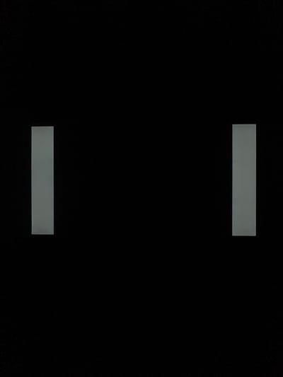 The image is a black and white photograph featuring two vertical grey rectangles against a stark black background. The rectangles are positioned symmetrically, one on the left side and the other on the right side of the frame, creating a sense of balance and space. The rectangle on the left is situated towards the lower left corner of the image, while the one on the right is placed towards the lower right corner. Both rectangles appear to be of similar size and are oriented vertically. The black background is uniform and devoid of any other discernible features, emphasizing the minimalist composition of the image. There is no indication of any specific location, including Nalazar, Uzbekistan. The image does not depict any people, actions, or interactions. It is purely an abstract composition of geometric shapes.