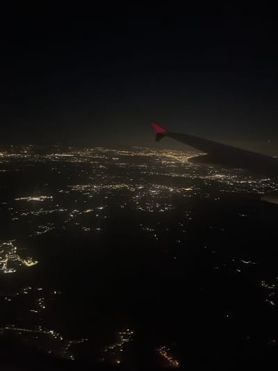 The image depicts an aerial view, likely taken at night, of what appears to be a coastline with scattered lights suggesting a city or town. The lights are a mix of white and yellow, indicating various sources like streetlights and building illumination. In the foreground, a dark shape with a red appendage or marker is visible, possibly part of the aircraft or drone from which the image was captured.
While the details are limited, the general characteristics of the coastline and the scattered lights potentially align with the coastal areas of Trevignano Romano, Italy, as it is situated along the shores of Lake Bracciano. The environment suggests a night-time setting, with an emphasis on the lights illuminating the settlement. Further analysis would be needed to confirm this location.