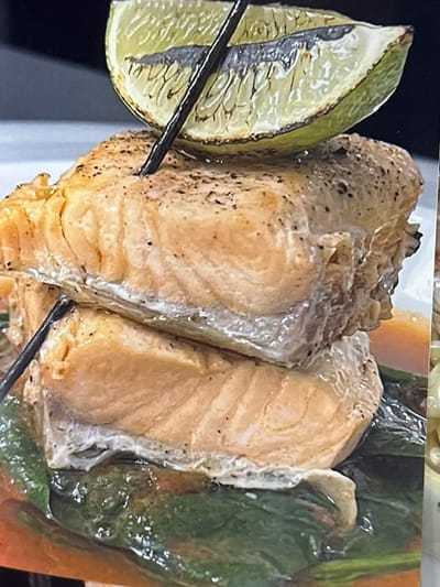 A close-up photograph depicts cooked salmon skewers featuring a lime wedge on one end and what appears to be a green vegetable, possibly a pepper, on the other. The salmon has a golden-brown surface, suggesting it has been grilled or pan-fried. The skewers appear to be metallic. The shot is tightly framed, with limited background details. There is no indication of the location being Новоглаголево, Russia.
