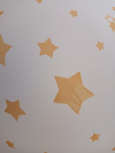 The image displays a textured white background with scattered orange star shapes. These stars vary in size and orientation, with some appearing solid and others with a more stenciled appearance. The lighting suggests a soft, diffused light source. There are no people, animals, or specific landmarks visible that would indicate a location in Marusino, Russia, or any other city. The image focuses solely on the pattern of the stars against the white surface.