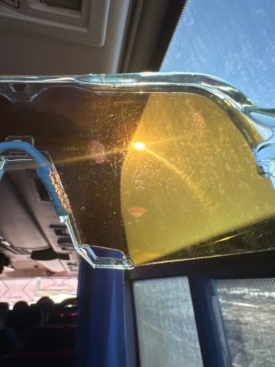A yellow, rectangular sun visor is positioned in the interior of a vehicle, obscuring a view of the outside. The visor is made of a translucent yellow material with a clear plastic frame. Light reflecting off the visor gives the impression of the sun, though it is not clear if this is the sun or an artificial light source. The interior of the vehicle, including the dashboard, is visible, suggesting a car or truck. The vehicle is presumed to be in the city of Челва, Russia based on the prompt.