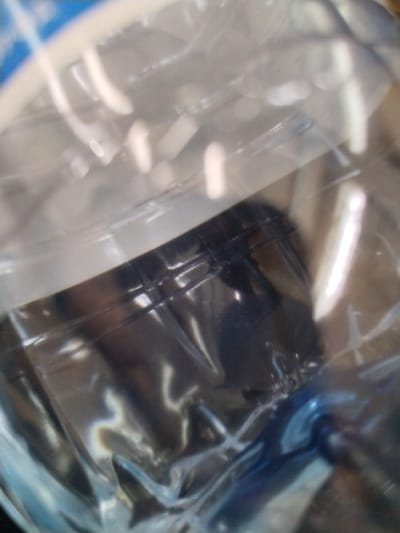 The image is a close-up, blurry shot of what appears to be a plastic bag containing some dark objects. The plastic is translucent and reflects light, creating bright highlights and obscuring details. There are no discernible features of a person, action, or interaction. The environment is not visible. The image does not contain any information about the location in the city of Гожскі сельскі Савет, Belarus.
