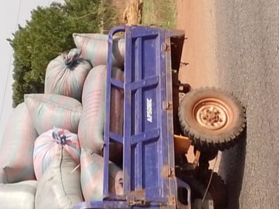 A blue truck, labeled "APSONIC", is loaded with large, white bags, possibly grain or agricultural products. It is parked on a paved road near some green foliage. The location is likely Dungu, Ghana.