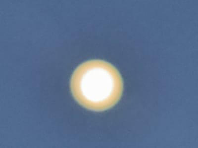 A bright, circular object, likely the sun, is centrally located in a clear, blue sky. The object is surrounded by a faint, yellowish halo. The sky appears to be a uniform, light blue, with no discernible clouds or other atmospheric phenomena. The image is an outdoor shot, and given the context of Gidan Waziri, Nigeria, it suggests a daytime scene. There are no people, buildings, or other objects visible in the frame.