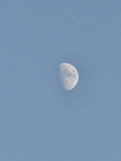 The image shows a crescent moon in a clear, pale blue sky. The moon is partially illuminated, revealing craters and surface details. The sky is uniformly colored with no clouds or other celestial bodies visible. The image is taken from a ground-level perspective, looking upwards. The location is Issy-les-Moulineaux, France. The scene is devoid of any human presence, buildings, or geographical features, focusing solely on the lunar object against the vast expanse of the sky.