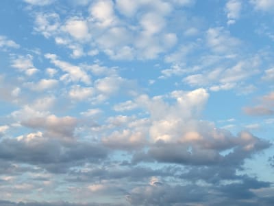 The image shows a sky filled with various types of clouds. Some are small, fluffy cumulus clouds, while others are larger, more layered stratus clouds. The sky is a clear blue, with the clouds casting shadows on each other in some areas. There is a subtle pinkish hue to some of the clouds, suggesting the sun may be low on the horizon or breaking through the clouds. The scene is devoid of any human presence or man-made objects. The image is a photograph of a natural sky formation. It is not possible to determine the specific location in Lyady, Russia from this image alone.