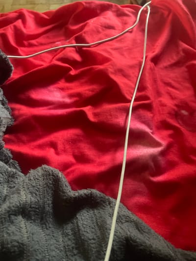 A light-colored cable is visible on a red, wrinkled fabric surface, partially obscured by a dark, textured fabric on the left side of the image. The scene is indoors and appears to be on a bed or similar surface, given the textures of the fabrics. No specific location in the city of Линёвка, Russia, can be determined from the visual information provided.