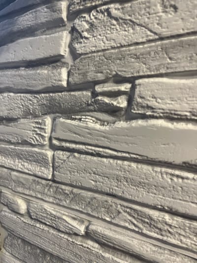 The image displays a close-up, angled view of a gray, textured stone wall. The stonework consists of irregularly shaped, rectangular blocks with rough surfaces and distinct grout lines between them. The lighting casts shadows, highlighting the texture and depth of the stone. There are no people or discernible objects other than the wall itself. The context of Abzakovo, Russia, is not visually evident in the image.