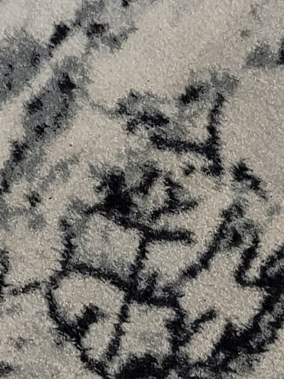 The image displays a close-up view of a carpet with a black and white abstract pattern. The texture appears plush and slightly uneven. The pattern consists of irregular, splotchy shapes in black against a cream-colored background. There is no discernible indication of a specific location within the city of Zlatopil, Ukraine, nor are there any people, subjects, objects, actions, or interactions visible in this macro photograph of the carpet's surface.