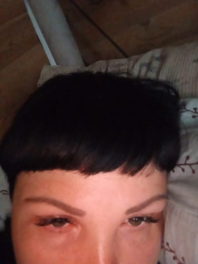 The image is a close-up, head-on shot of a person's face, focusing on their eyes and forehead, with their dark hair prominently displayed. The background appears to be a bed with striped bedding and a hint of a wooden surface. The lighting is dim. The image does not provide any information about the location in the city of Засопка, Russia.
