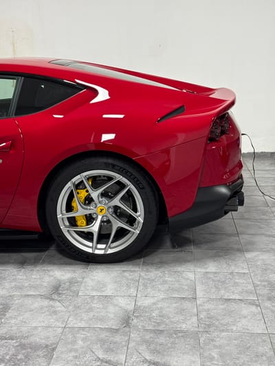 The image shows the rear right side of a red Ferrari coupe parked on a tiled floor in a garage. The car is facing towards the left of the image. The car is in excellent condition. The car is parked on a tiled floor made of square tiles. The tile floor is a gray color with a slightly textured surface. The rear tire is a Michelin Pilot Sport 4S tire. The rim of the tire is silver and has a black Ferrari logo in the center. The rear brake caliper is yellow. The car has a black exhaust pipe. The car has a black rear spoiler. There are no people present in the image. The image was taken in Daliyat al-Karmel, Israel. The location is based on the provided coordinates.