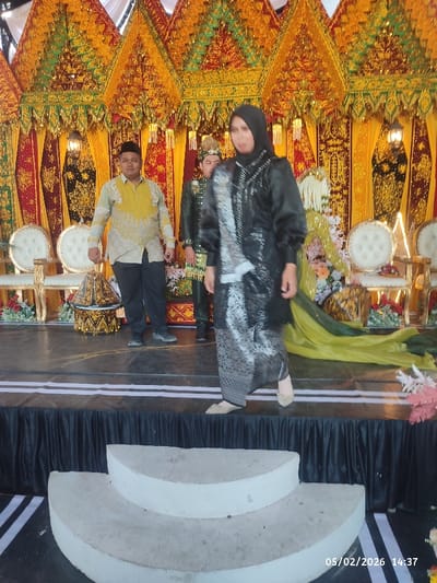 Three individuals stand on a raised platform adorned with ornate decorations and chairs. A woman in a black and silver outfit is walking forward. Behind her, a man in a green military-style suit stands. To the left, another man in a yellow shirt and black pants stands facing forward. The platform has a black fabric covering, and in front, there are white, semi-circular steps leading up to it. A date stamp is visible in the bottom right corner.