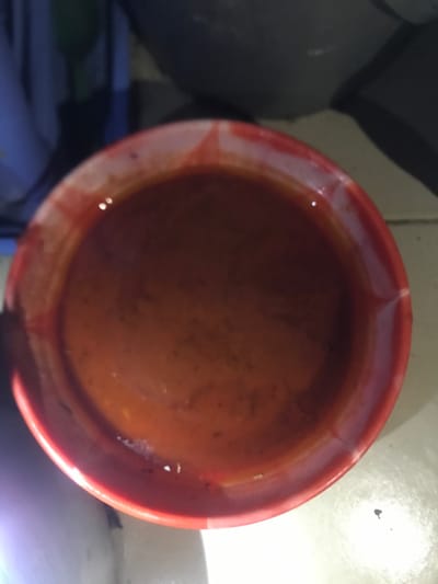 The image shows a red bowl filled with a thick, reddish-brown liquid. The bowl is made of ceramic and has a white rim. The liquid appears to be a sauce or soup. The image is taken from an overhead perspective, and the bowl is the only subject in the frame. The image was likely taken indoors. The location of the photo is in Umudike, Nigeria, based on the provided coordinates.