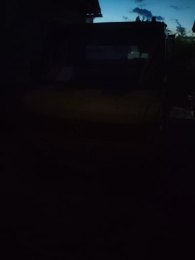 The image is a dark, grainy, and slightly blurry photograph taken at dusk or night. The foreground is almost entirely black, obscuring any details. In the upper portion of the image, a dark structure, possibly a building or a large vehicle, is visible against a twilight sky with scattered clouds. The sky transitions from a deep blue to a lighter shade at the horizon. There are faint reflections on the dark structure, suggesting it might be made of a glossy material. The overall impression is one of low light conditions and limited visibility. The location in Pinsk, Belarus, cannot be determined from the visual information provided in the image.