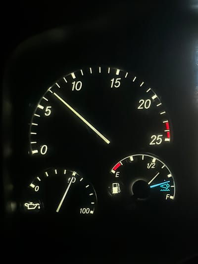 The image shows a close-up of a vehicle's dashboard at night. The dashboard features three illuminated gauges. The largest gauge, likely a speedometer, displays markings from 0 to 25, with a needle pointing slightly past the 10 mark. To the lower left, a smaller gauge, presumably an oil pressure or temperature gauge, shows markings from 0 to 100, with a needle indicating a value around 40. A symbol of an oil can is also visible near the 0 mark. To the lower right, another gauge, representing a fuel level, has markings for "E" (empty) and "F" (full), with a needle pointing past the "1/2" mark towards "F". A fuel pump icon is located near the "E" mark, and a boat icon with waves is visible near the "F" mark, possibly indicating a fuel level warning or a specific fuel type. The overall environment is dark, suggesting it is nighttime, and the gauges are lit by the vehicle's interior lighting. There are no people or other objects visible in the frame. This scene is not specifically located in Wildwood, United States; it is a generic image of a vehicle's dashboard.