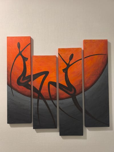 The image depicts a four-panel abstract artwork hanging on a textured, off-white wall. The artwork features stylized, silhouetted figures in black against a gradient of orange and yellow, suggesting a sunset or fiery sky. The bottom portion of each panel is a dark gray, textured area that appears to represent the ground or water. The panels are arranged in a horizontal line, with the first two panels slightly shorter than the last two. The overall style is minimalist and evocative, with flowing lines and bold colors. The image is captured from a slightly angled perspective, highlighting the texture of both the artwork and the wall. There is no indication of the specific location within Vyshhorod, Ukraine, as the image focuses solely on the artwork and the wall it is mounted on.