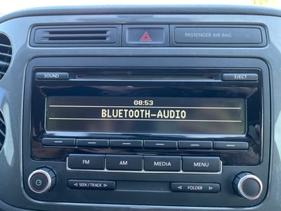 The image shows a close-up view of a car's central console, specifically the infotainment system and surrounding controls. The screen displays "08:53" and "BLUETOOTH-AUDIO" in pixelated text. Below the screen are several buttons labeled "SOUND", "EJECT", "FM", "AM", "MEDIA", and "MENU", along with directional arrows for seeking tracks or folders. A circular power button with a 'G' symbol is visible on the left, and a similar dial is on the right. Above the screen, there are air vents, a hazard light button with a red triangle symbol, and a "PASSENGER AIR BAG OFF" indicator. The console is dark grey and appears slightly dusty. The scene is devoid of people or any elements that would indicate its location in Chervonyi Lan, Ukraine.