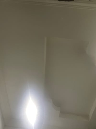 The image depicts an interior view of a room with white walls and a decorative ceiling element. A bright light source is visible in the lower right portion of the frame. The location of the image is impossible to determine with the image as the location in the city of Ebo, Nigeria, is not visible. There are no people, visible subjects, interactions, or specific actions visible in this photograph.