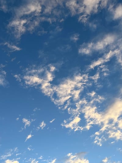 The image shows a clear blue sky with scattered white clouds. The clouds vary in size and shape, some appearing wispy and stretched, others more dense and puffy. The photo was taken from a low angle, looking upwards. The location of the photo is El Bañado, Argentina, as inferred from the prompt.