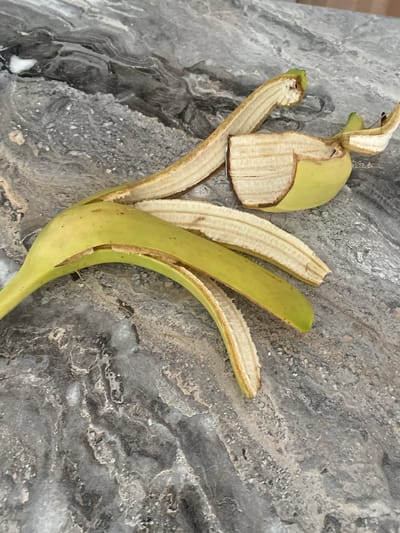 A partially peeled green banana lies on a grey, marbled surface. The banana peel is separated into several pieces, revealing the pale, fibrous interior of the fruit. The surface appears to be a countertop. The image does not contain information that would indicate a specific location in the city of Udachny, Russia.
