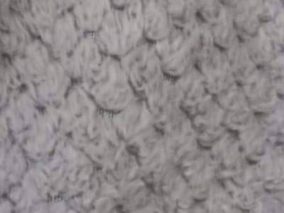 This is a close-up, abstract shot of a textured, light grey material, likely a textile. The texture is characterized by a series of raised, looped or tufted elements that create a somewhat scaly or quilted appearance. The lighting is diffused, casting soft shadows that highlight the three-dimensionality of the surface. There are no discernible subjects, objects, or a clear scene or setting. The image does not depict any activity or event. There are no visible cues for time of day, weather, or specific location. No text is visible in the image. The overall impression is one of tactile softness and a repeating pattern. The crops provided offer slightly different perspectives and magnifications of the same textured surface, but do not reveal any additional information about the content or context.