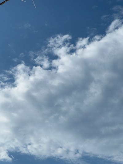 The image depicts a sky with clouds. There are two thin, white, rod-like objects partially visible in the upper left corner of the frame, extending downwards and to the right. They appear to be attached to something out of frame. The sky is a deep blue, with scattered white and gray clouds. The clouds are dense and fluffy, with some appearing darker and more shadowed than others. The overall impression is of a partly cloudy day. There are no people, animals, or structures visible within the frame, and the scene appears to be outdoors. The location is identified as Golubitskaya, Russia.
