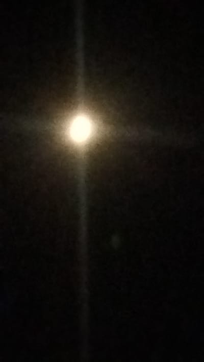 The image displays a dark, nighttime scene with a bright, round object, likely the moon, in the upper-center portion. A vertical beam of light emanates from this object, extending downwards. The background is black, suggesting a sky. There are no discernible people, structures, or specific landmarks indicative of Kostiantynivka, Ukraine. The overall impression is that of a celestial event captured in a low-light environment.