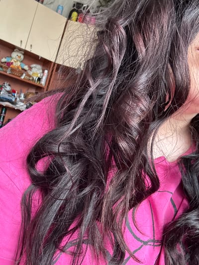 The image shows a close-up of dark, wavy hair against a pink fabric background. A small section of a beige cabinet with drawers containing various small objects is visible in the lower-left corner. There is no evidence to place the image in Dobrovnitsa, Bulgaria.