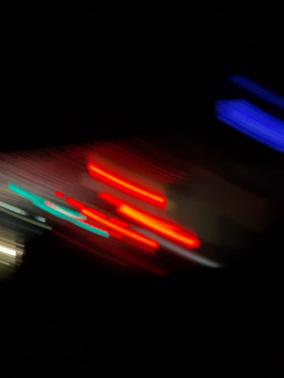 The image shows blurred streaks of blue, red, and teal lights against a dark background. The streaks are diagonal and appear to be captured with a long exposure or while in motion. Based on the prompt's instructions, the location is Kursk, Russia. However, without clearer imagery, any further detail or forensic information will be speculation. No people or objects (other than the lights) are discernible. No actions or interactions can be described. The environment is dark.