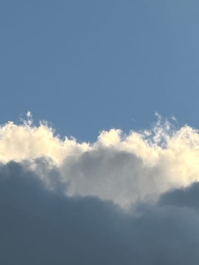 The image depicts a portion of the sky above Voeikovo, Russia. The upper half of the image is dominated by a clear, blue sky. The lower half features a layered arrangement of clouds. The topmost layer of clouds is wispy and white, with some appearing illuminated with a yellowish hue, suggesting sunlight. Below these, a thicker, gray cloud formation extends across the frame, with its upper edge showing some lighter, textured areas where it meets the brighter clouds. The lowest visible portion of the image is a darker, more solid gray cloud layer. The scene is devoid of any human presence, structures, or discernible objects, focusing solely on the atmospheric conditions.