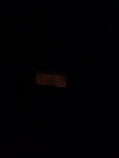 A dark image shows a close-up of a coin with a ridged edge. The coin is oriented horizontally in the center of the frame. The lighting is dim, creating a shadowed effect. The image is likely taken in a dimly lit environment, possibly indoors. There are no people or any other identifiable objects in the scene.
